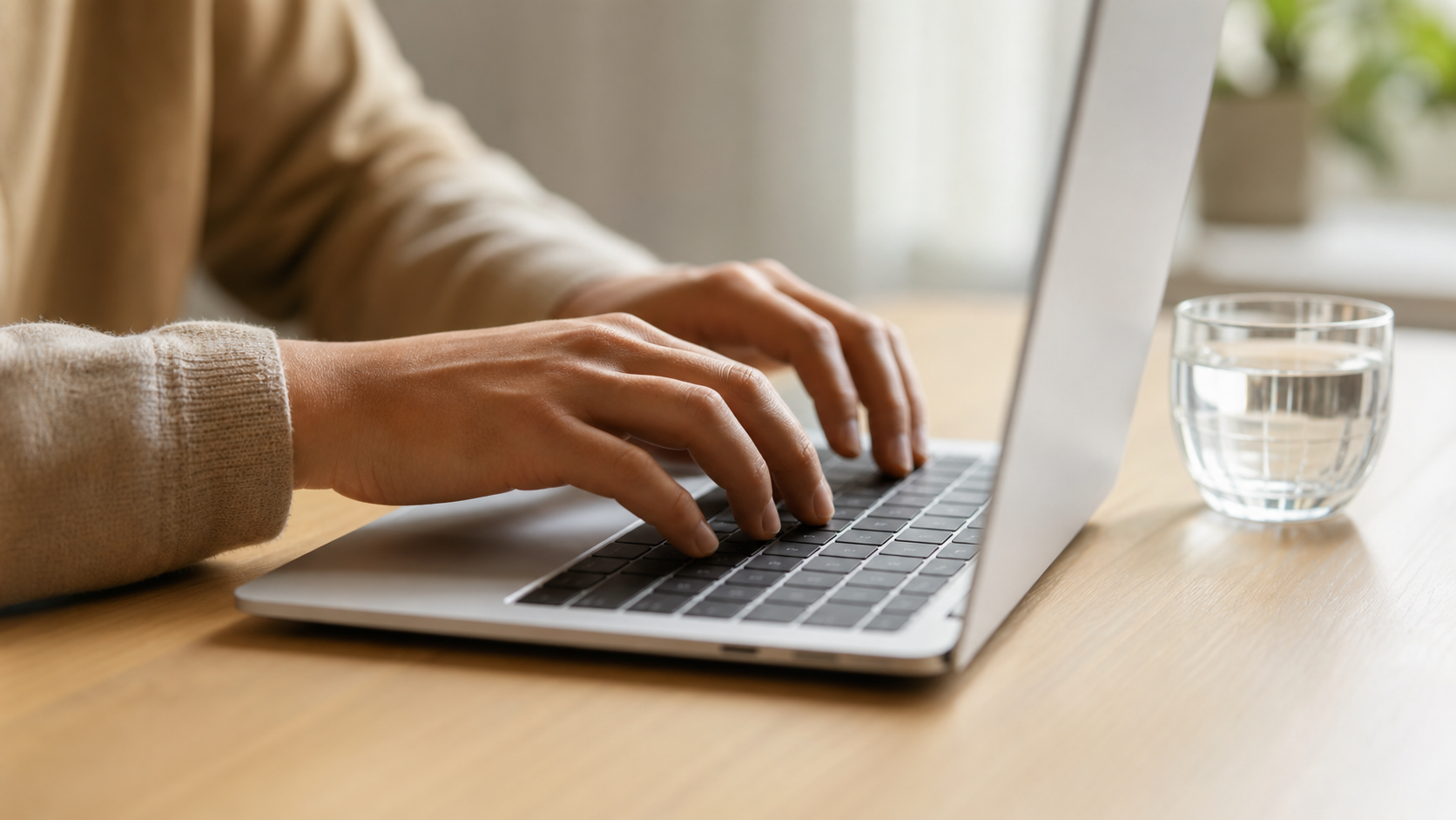 hands typing on a laptop keyboard at a clean minimal workspace, warm natural light